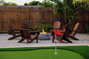 A patio area with Adirondack chairs, a fire pit, and a flag. - Heated Pool + Spa | Mini Golf | 5BR Coastal Retreat Near Anna Maria Island (Bradenton)