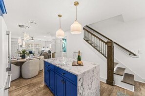 A modern kitchen with a marble island, blue cabinets, pendant lighting, and a wooden staircase. - Editorial Townhome on Quiet Beach • 3mi to 30A (Panama City Beach)