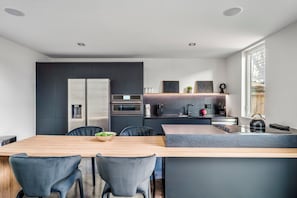 A modern kitchen with a central island, dark cabinetry, and a dining area with chairs.