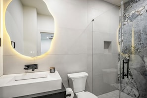 Une salle de bain moderne avec un lavabo blanc, des toilettes et un espace douche.
