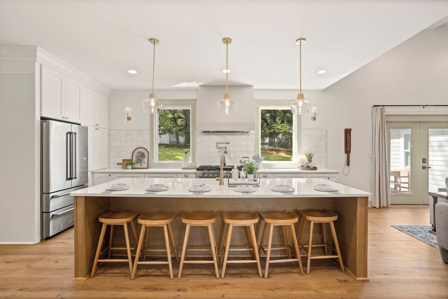 Una cocina moderna con una isla central, taburetes de bar, electrodomésticos de acero inoxidable e iluminación colgante.