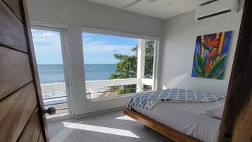Een slaapkamer met een bed, een plafondventilator, een schilderij en uitzicht op de oceaan.