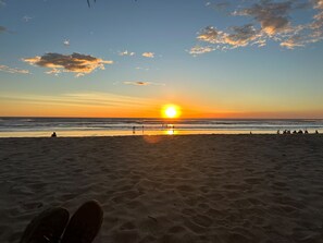 A beach with a sunset, sand, and a few people.