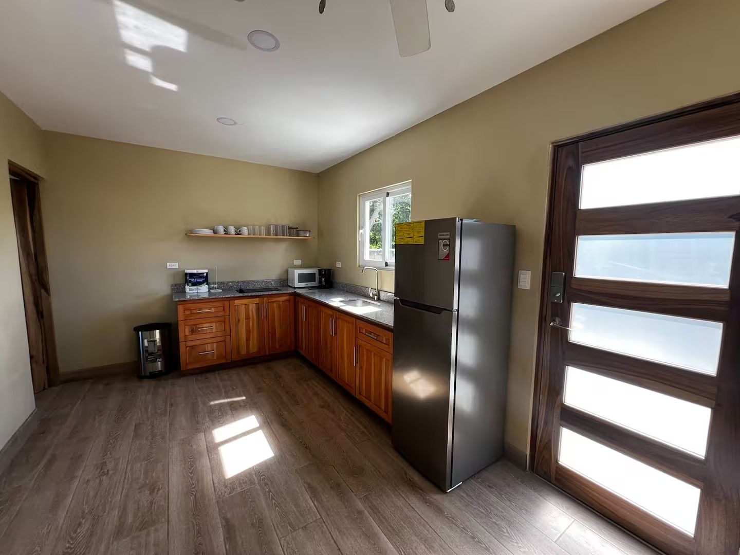 A kitchen with wooden cabinets, a stainless steel refrigerator, and a window with blinds.