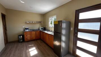 A kitchen with wooden cabinets, a stainless steel refrigerator, and a window with blinds.
