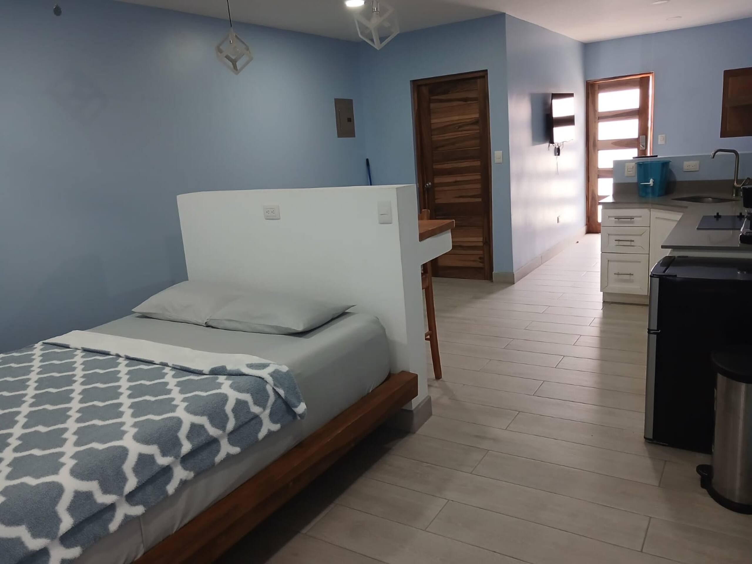 A bedroom with a bed, a desk, and a kitchenette.