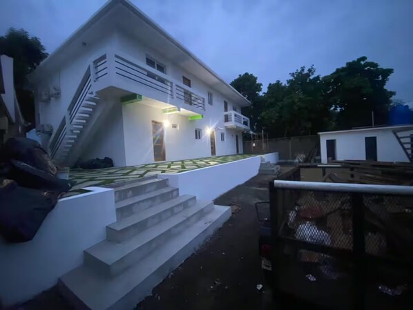 A modern two-story house with a staircase leading to the entrance, a fenced yard, and a small adjacent building.