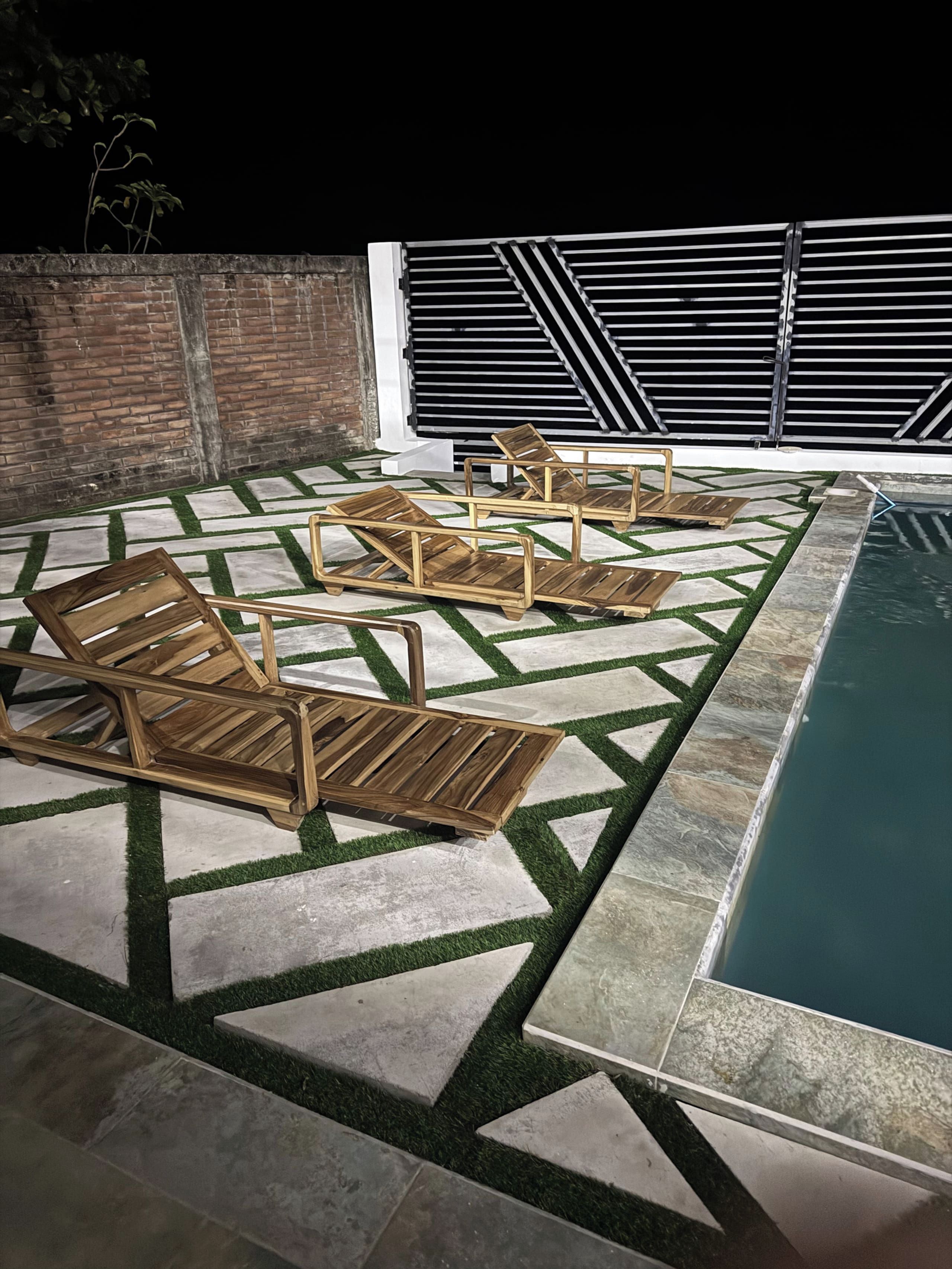 Un espace aménagé au bord de la piscine, avec une terrasse au motif géométrique, des chaises longues en bois et un mur en briques.