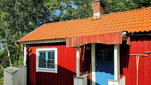 Ein rotes Holzgebäude mit einer blauen Tür und einem Fenster, einer kleinen Veranda und einem Schornstein.