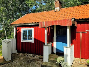 A red wooden building with a blue door and window, a small porch, and a chimney. - Renovated guesthouse with courtyard in Ljungskile (Västra Götalands län)