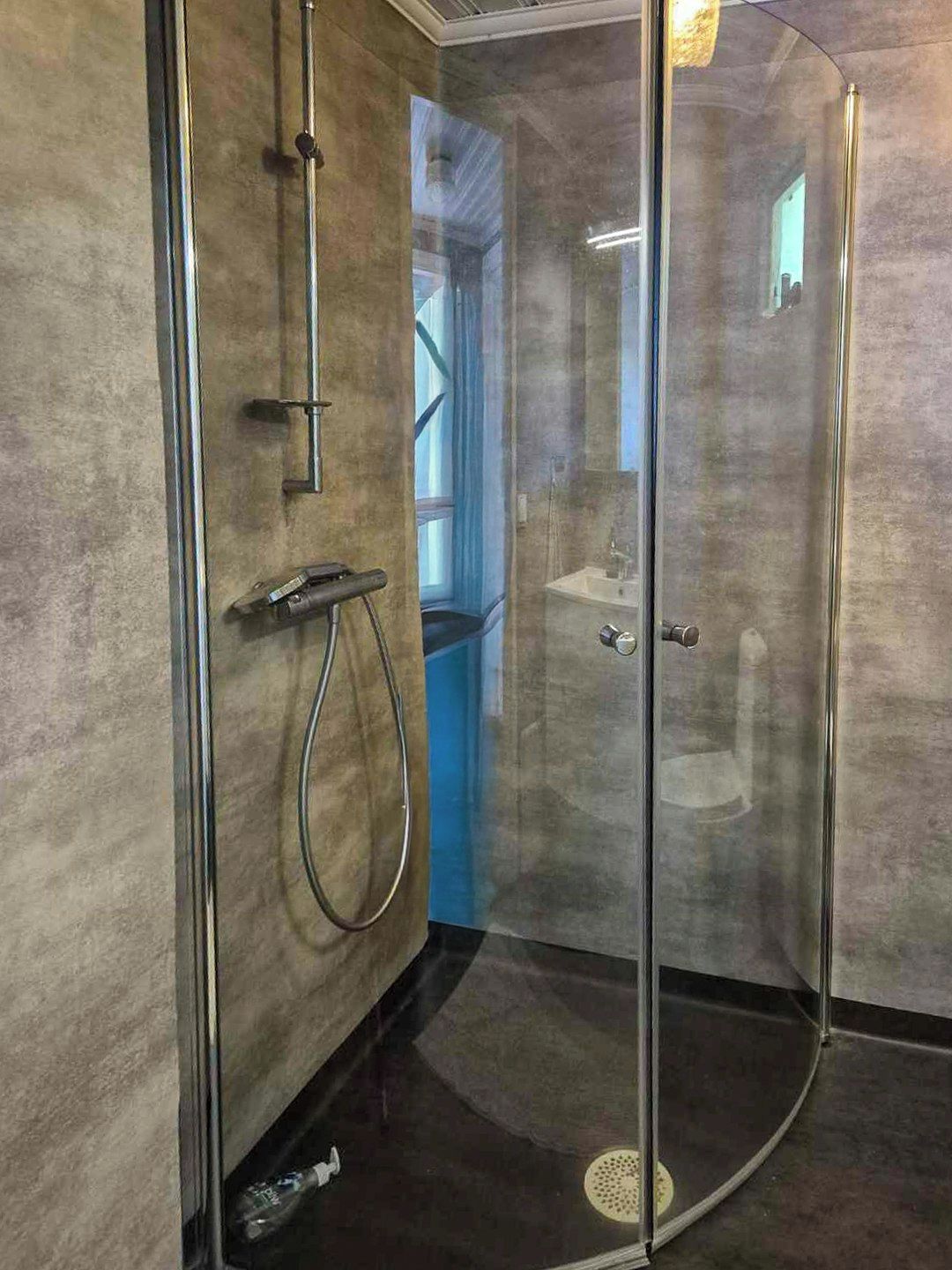 A glass-enclosed shower with a handheld showerhead and a wall-mounted faucet.