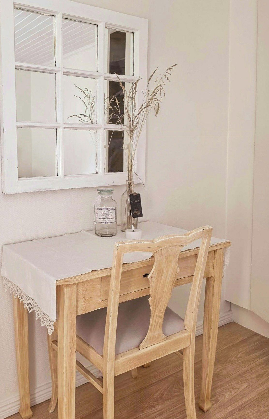 Une table à manger en bois, recouverte d’une nappe blanche, avec un vase contenant des plantes séchées et une bougie posée sur la table.