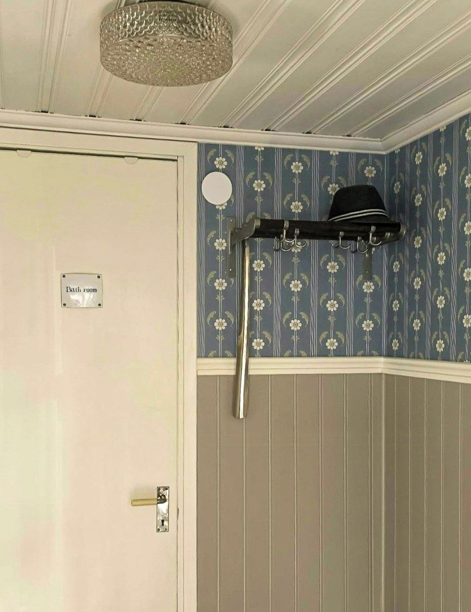 Una habitación con una puerta que indica 'baño', un perchero y un papel tapiz estampado.