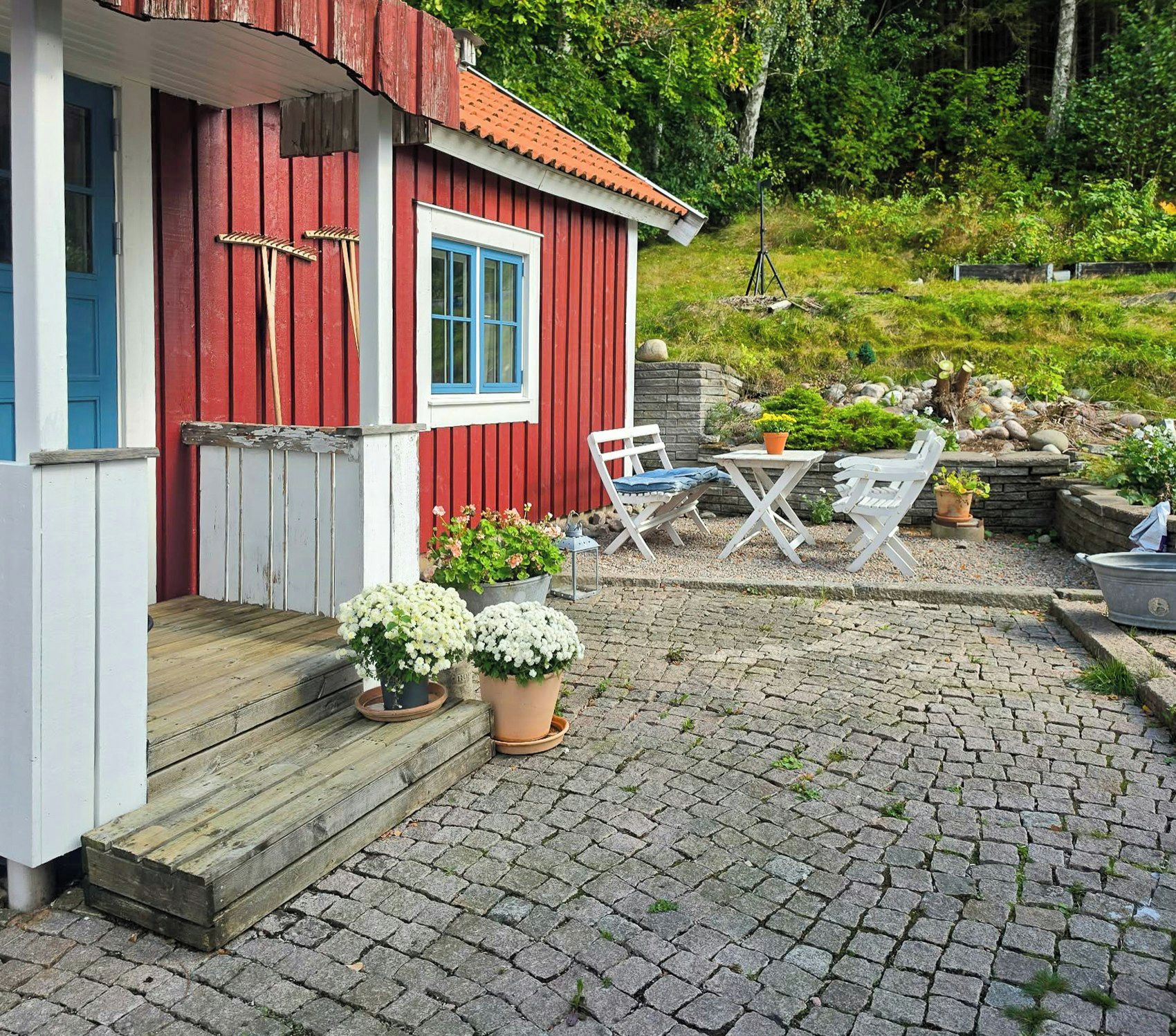 A red wooden house with a blue door and window, a wooden porch, and outdoor seating.