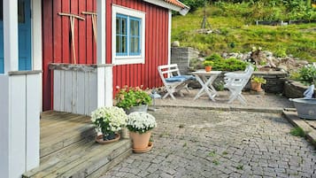 A red wooden house with a blue door and window, a wooden porch, and outdoor seating.