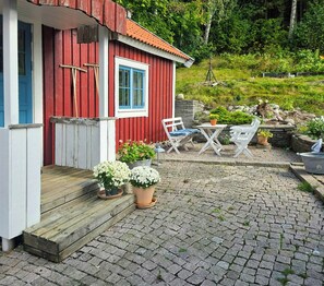 A red wooden house with a blue door and window, a wooden porch, and outdoor seating.