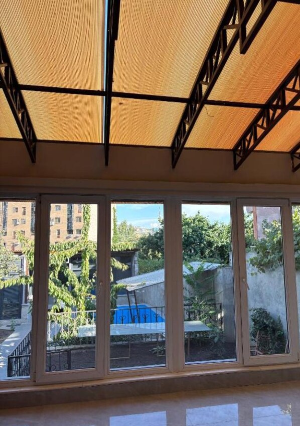A room with large windows, a ceiling with a woven pattern, and a view of a blue structure outside. - Alikhanyan House (Yerevan)