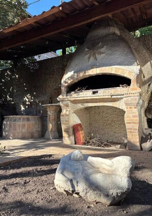 Un horno de piedra al aire libre con estructura de ladrillo, una escultura de piedra y una mesa de madera.