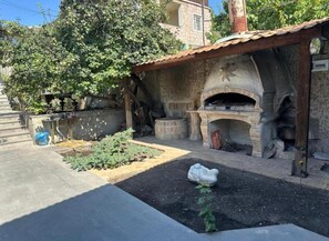 An outdoor kitchen area with a stone oven, a raised garden bed, and a stone statue. - Alikhanyan House (Yerevan)