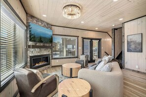 A modern living room with a fireplace, comfortable seating, and large windows. - LUX Cabin/1mi to Parkway/Golf Suite/Indoor Pool (Pigeon Forge)