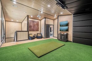A room with a green artificial turf floor, wooden walls, a ceiling fan, and a large painting on the wall. - LUX Cabin/1mi to Parkway/Golf Suite/Indoor Pool (Pigeon Forge)