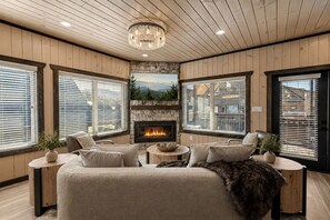 A cozy room with a fireplace, wooden walls, and large windows. - LUX Cabin/1mi to Parkway/Golf Suite/Indoor Pool (Pigeon Forge)