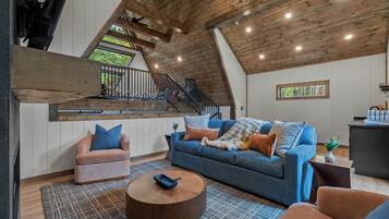 A loft-style living room with a high ceiling, wooden beams, a blue sofa, a pink armchair, and a round coffee table.