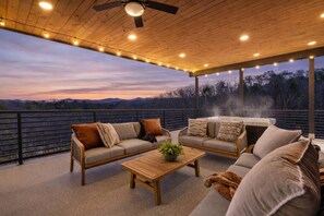 A covered outdoor seating area with a sofa, armchairs, and a table, overlooking a scenic landscape. - Sleeps 18/Rooftop/Golf Suite/Indoor Pool/Hot Tub (Pigeon Forge)
