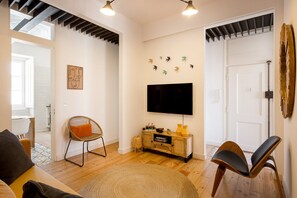 Un salon équipé d’un téléviseur à écran plat, d’un fauteuil en osier, d’une armoire en bois et d’une porte avec un cadre en bois.