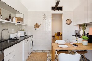 Une cuisine moderne équipée d’un lave-linge intégré, un coin repas avec une table en bois et un espace de vie avec un canapé.