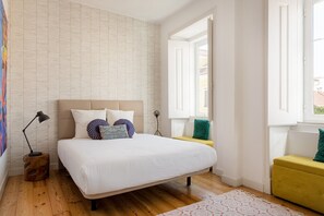 Ein Schlafzimmer mit einem Bett, Nachttischlampen, einem Fenster und Blick ins Freie.