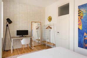 Une chambre à coucher avec un lit, un bureau avec un ordinateur, une chaise, une armoire et un tableau accroché au mur.