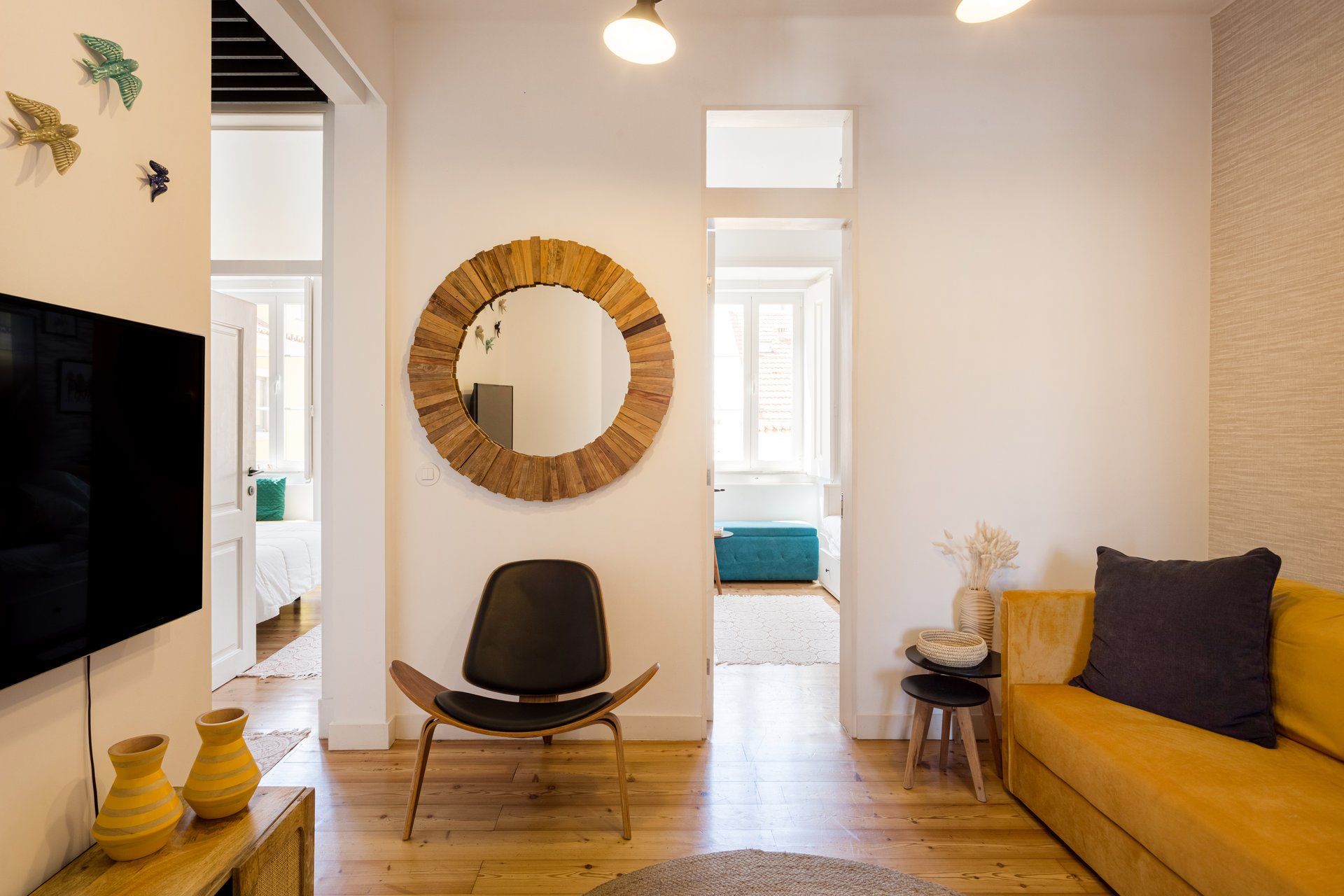 Un salon moderne avec un miroir rond, un fauteuil noir, un canapé jaune et un téléviseur à écran plat.