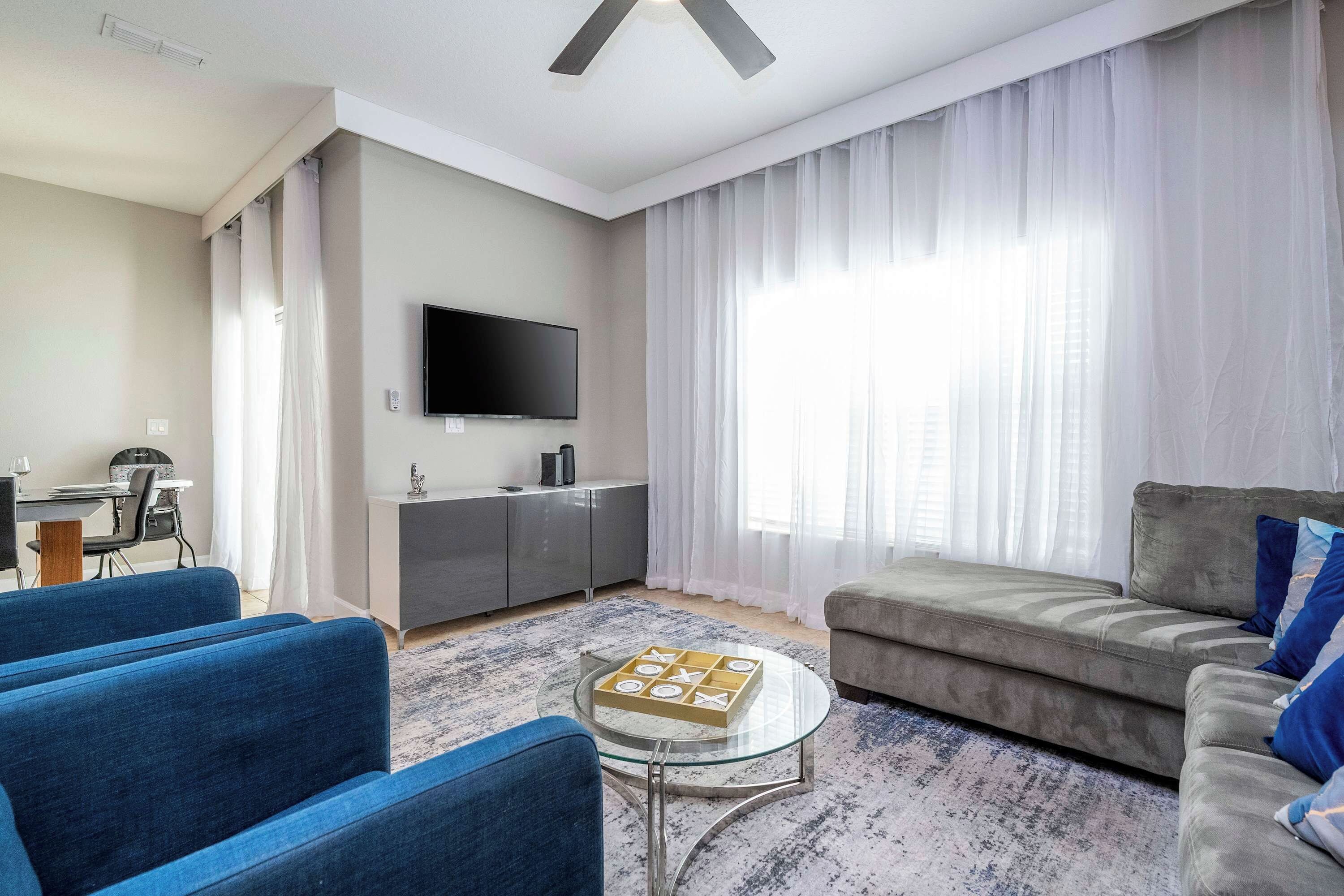 Ein modernes Wohnzimmer mit einem Flachbildfernseher, einem grauen Sofa, blauen Sesseln und einem Glastisch.