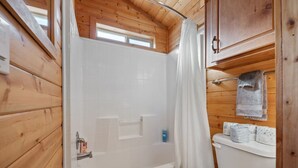 A wooden cabin bathroom with a bathtub, toilet, and a window above the shower.