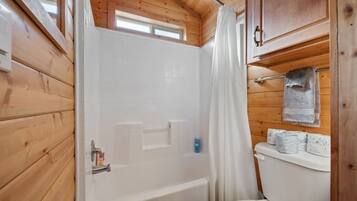 A wooden cabin bathroom with a bathtub, toilet, and a window above the shower.