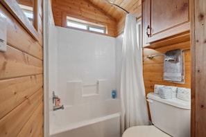 Et badeværelse i en træhytte med badekar, toilet og et vindue over brusenichen.