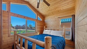 A wooden cabin room with a bed, windows, and a view of the outdoors.