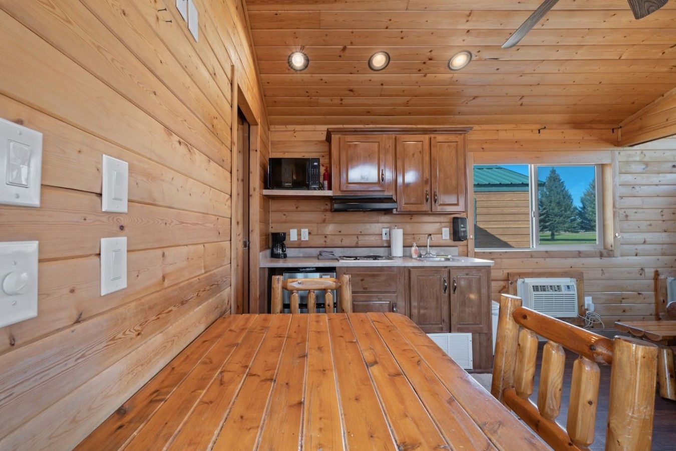 Un interior de madera con área de cocina, que incluye armarios, un microondas y una mesa de comedor con sillas.