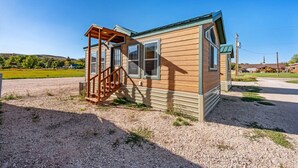 A small wooden cabin with a porch and a gravel driveway.