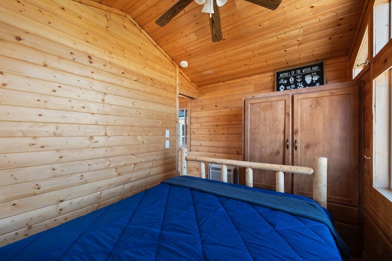 Habitación de cabaña de madera con cama, ventilador de techo y un letrero en la pared.