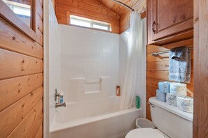 Et badeværelse i en træhytte med badekar, toilet og en hylde med toiletpapir og toiletartikler.