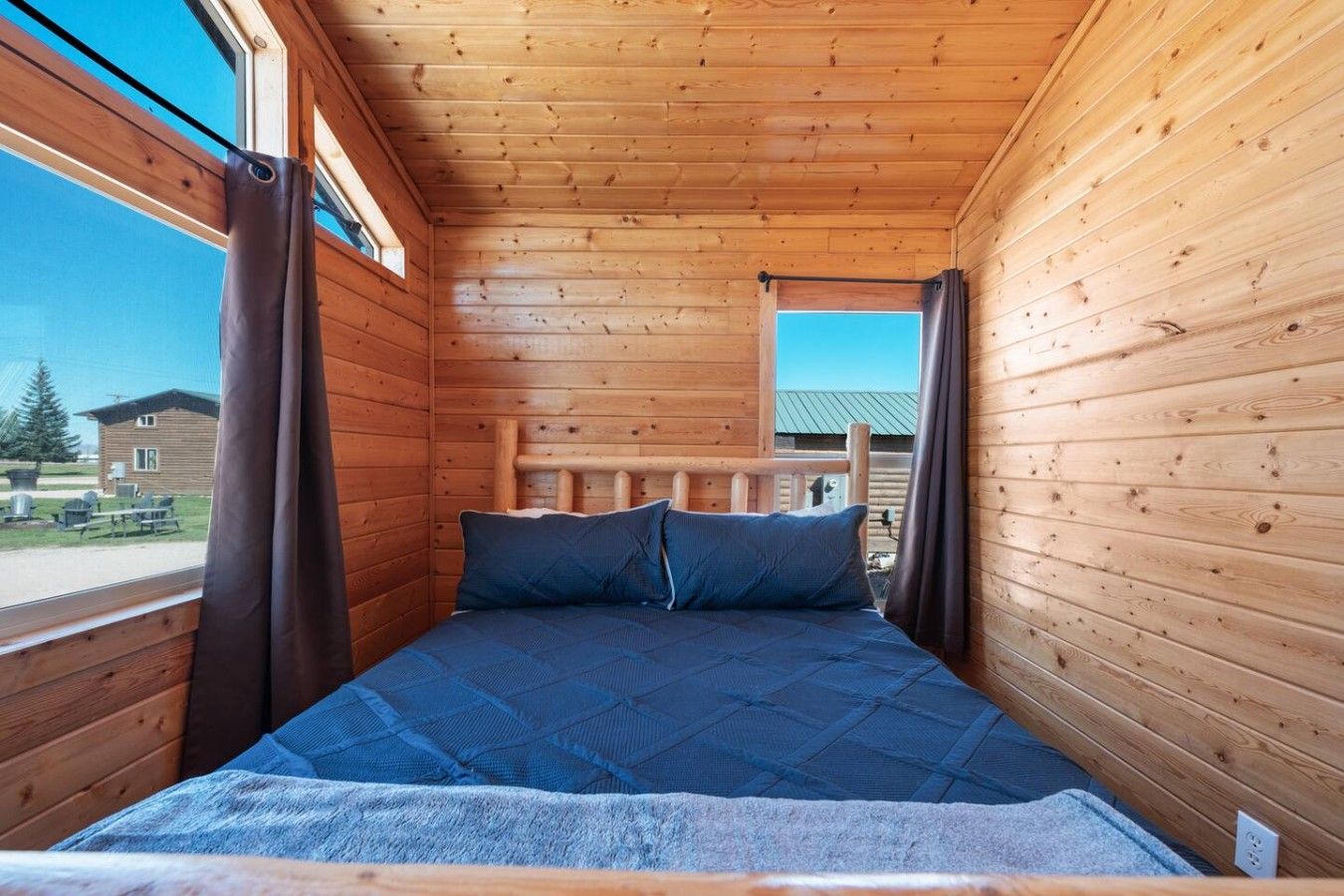 Une pièce de cabane en bois comprenant un lit, des rideaux et une fenêtre donnant sur un bâtiment.