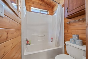 Et badeværelse i en træhytte med badekar, toilet og bruseforhæng.