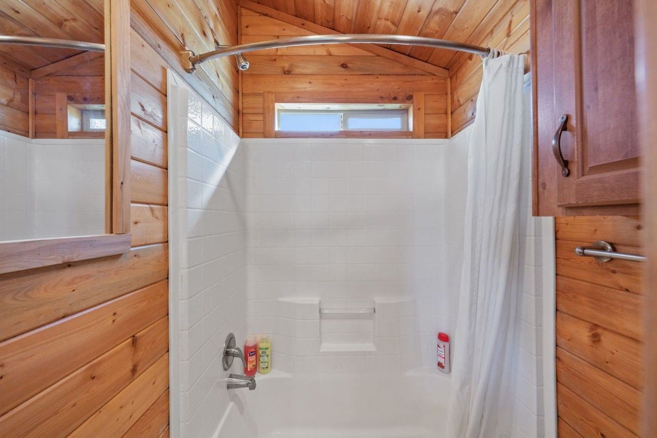 A wooden cabin bathroom with a shower, a window, and a towel rack.
