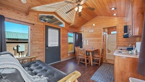 A log cabin interior with a dining area, kitchenette, and a living room with a sofa. - #K305 Quail Cabin - AC, Fire Pit & BBQ! (Saint Charles)