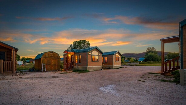 A rustic cabin with a dirt driveway, a wooden barn, and a small house with a porch. - #K305 Quail Cabin - AC, Fire Pit & BBQ! (Saint Charles)