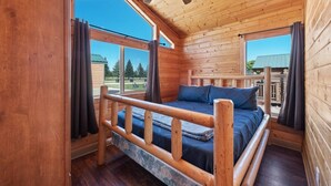 A wooden cabin room with a bed, a ceiling fan, and large windows. - #K305 Quail Cabin - AC, Fire Pit & BBQ! (Saint Charles)
