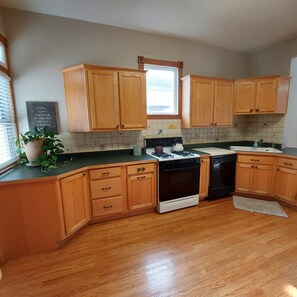 A kitchen with wooden cabinets, a stove, a dishwasher, and a window. - Spacious Gem Sleeps 10, Centrally Located, & 10 Min From Downtown Louisville (New Albany)