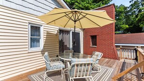 Een terras met een tafel en stoelen, een zonnescherm en een vuurplaats van baksteen.